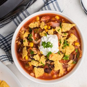 Overhead shot of slow cooker southwestern chicken tortilla soup with tortilla chips and sour cream with fresh cilantro.