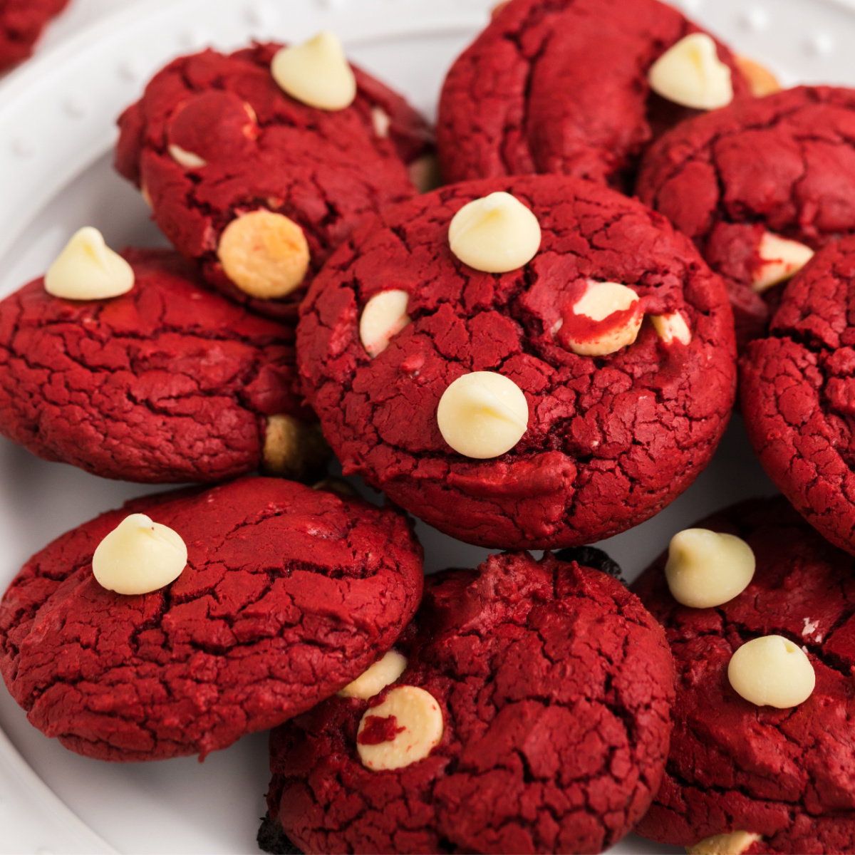 red velvet cake mix cookies with white chocolate chips stacked on a white plate.