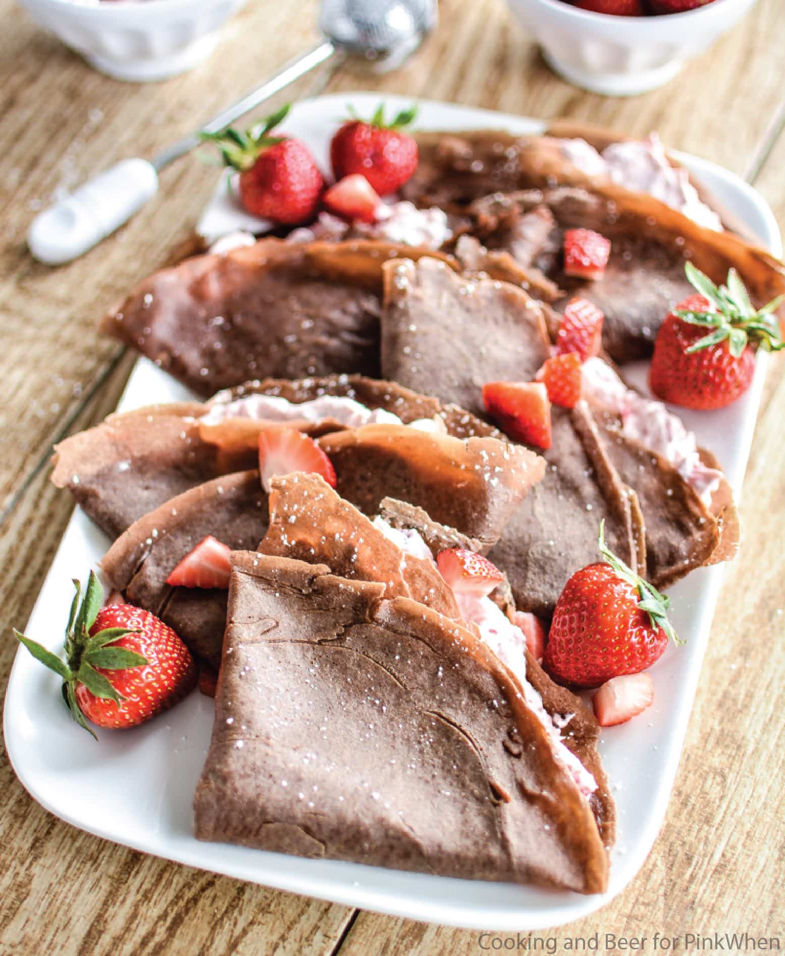 Strawberry Cheesecake Chocolate Crepes on a white plate garnished with strawberries and confectioner's sugar. 