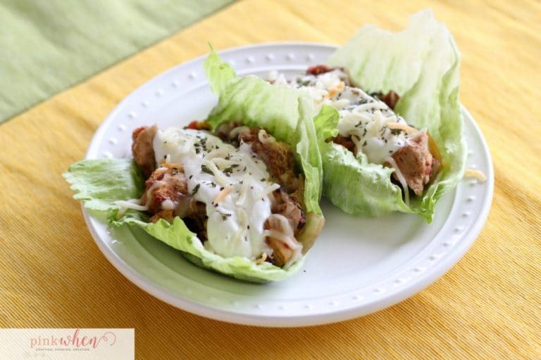Chicken Crock pot Tacos on a bed of lettuce and smothered in sour cream and cheese on a white plate.