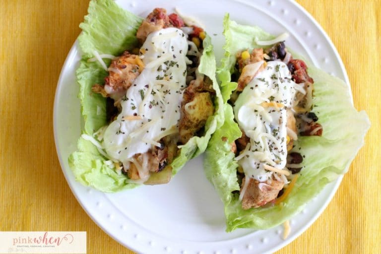 Chicken Crock Pot Tacos on a bed of lettuce, white plate, with a dollop of sour cream and cheese