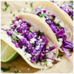 Slow Cooker Salsa Verde Chicken Tacos on paper with lime and crumbled cheese.