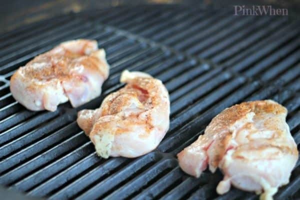 chicken breasts on the grate of a charcoal grill.