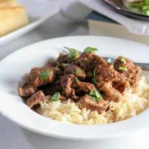 Juicy beef tips served on a bed of rice in a white bowl.