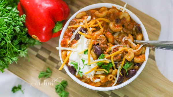 Instant Pot Chili Mac on a cutting board in a white bowl with toppings. 