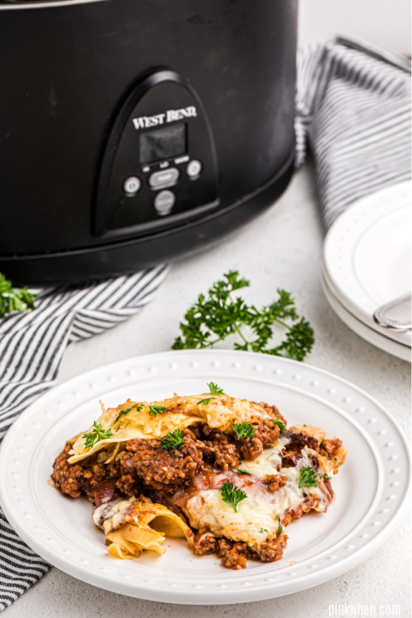 Lasagna on a plate with crockpot in the background.