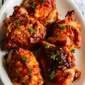 bbq chicken on a white plate and garnished with parsley.