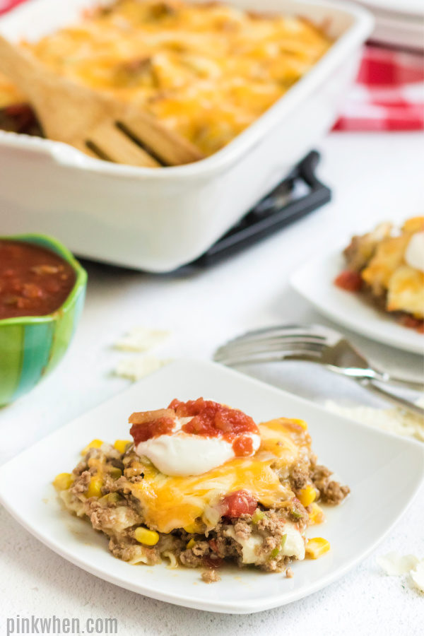 Taco casserole scooped onto a serving plate with sour cream and salsa. 