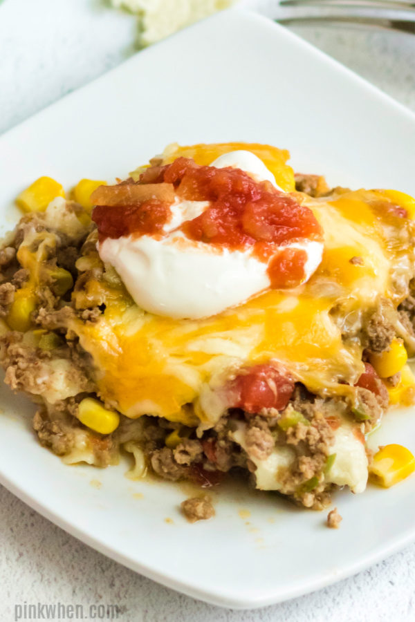 Taco casserole scooped onto a plate with sour cream and salsa. 