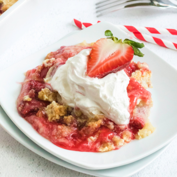 Slice of strawberry dump cake on a plate with whipped cream and strawberry on top.
