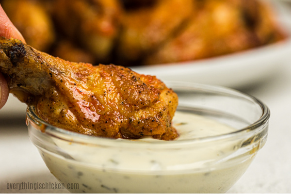 Chicken wing being dipped in ranch dressing. 