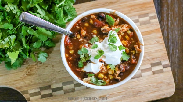 Bowl of chicken chili topped with sour cream and garnished.