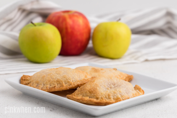 Apple hand pies on a plate with apples in the background.