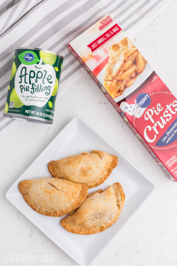 Apple hand pies on a plate with canned apple filling and a box of pie crusts.