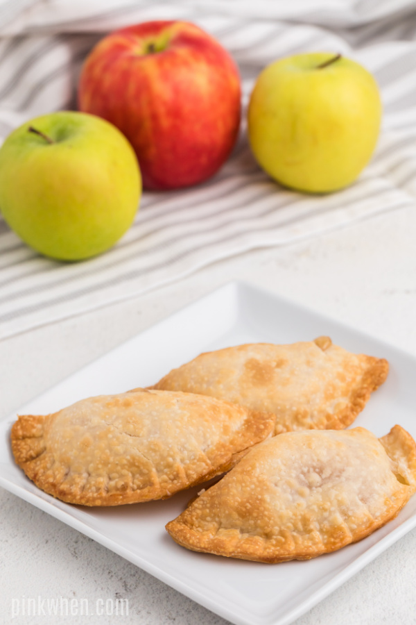 Apple hand pies on a white plate with apples in the background.