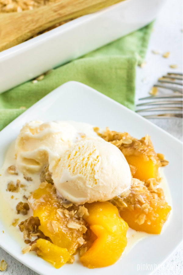 White plate served with peach crisp and ice cream.