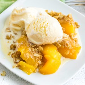 Peach crisp on a white plate with melted ice cream.