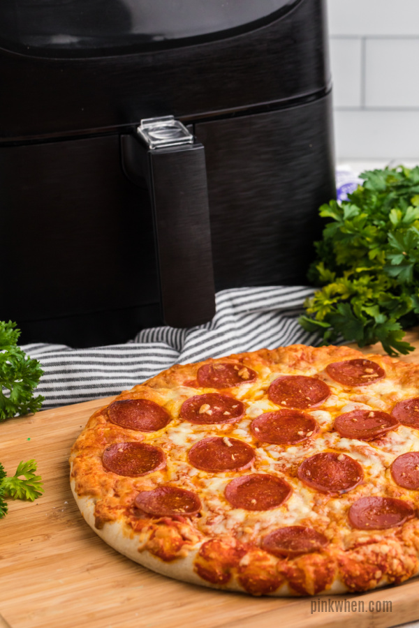 Pizza on a cutting block in front of an air fryer. 