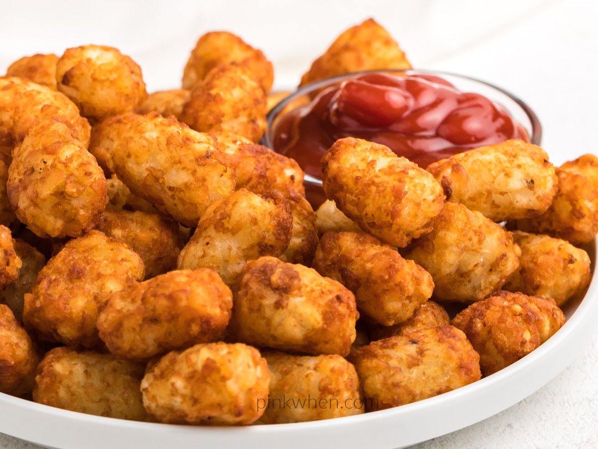 Tater tots on a white plate served with ketchup. 