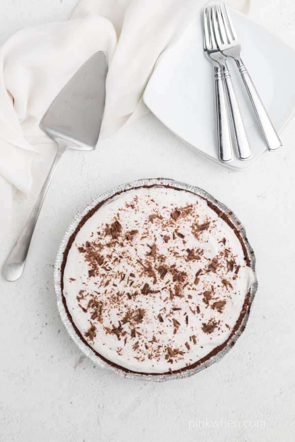 Chocolate Cream Pie on a white table with a pie cutter, plates, and forks. 