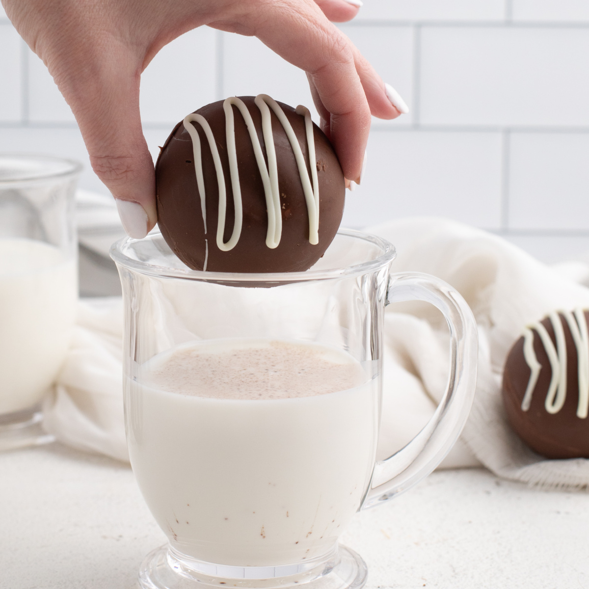 Hot chocolate bomb being placed into a clear glass of white milk