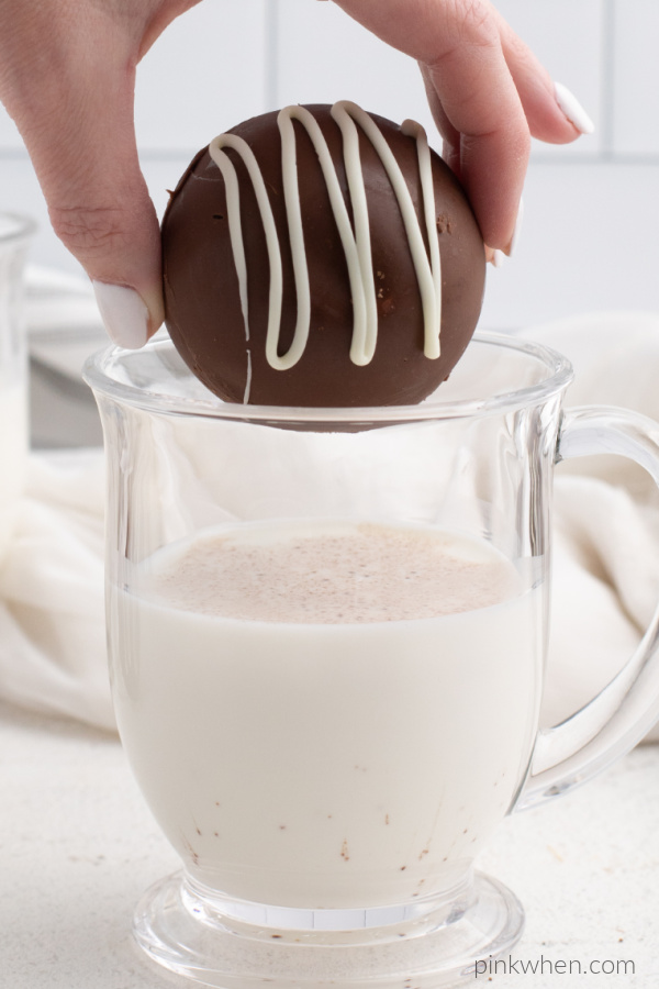 Hot cocoa bomb about to be dropped in a glass of hot milk.