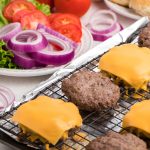 Baked hamburger patty's on a baking sheet with hamburger toppings in the background.