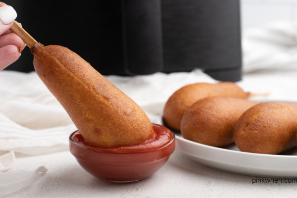 Full sized Corn dog being dipped in a small bowl with ketchup. 