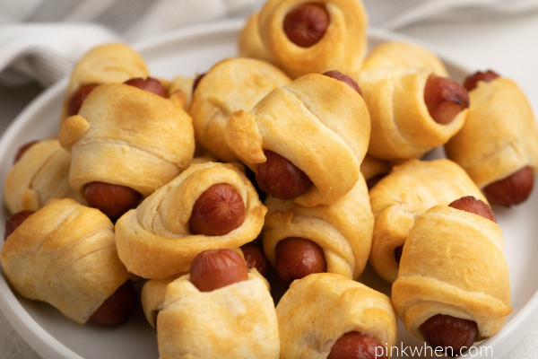 Cocktail sausages wrapped and cooked in crescent pastry dough on a white plate.