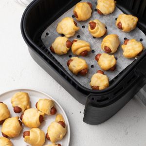 Crescent dogs in an Air Fryer basket and on a white plate.