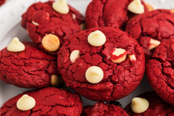 Red velvet cookies with white chocolate chips stacked on a white plate.