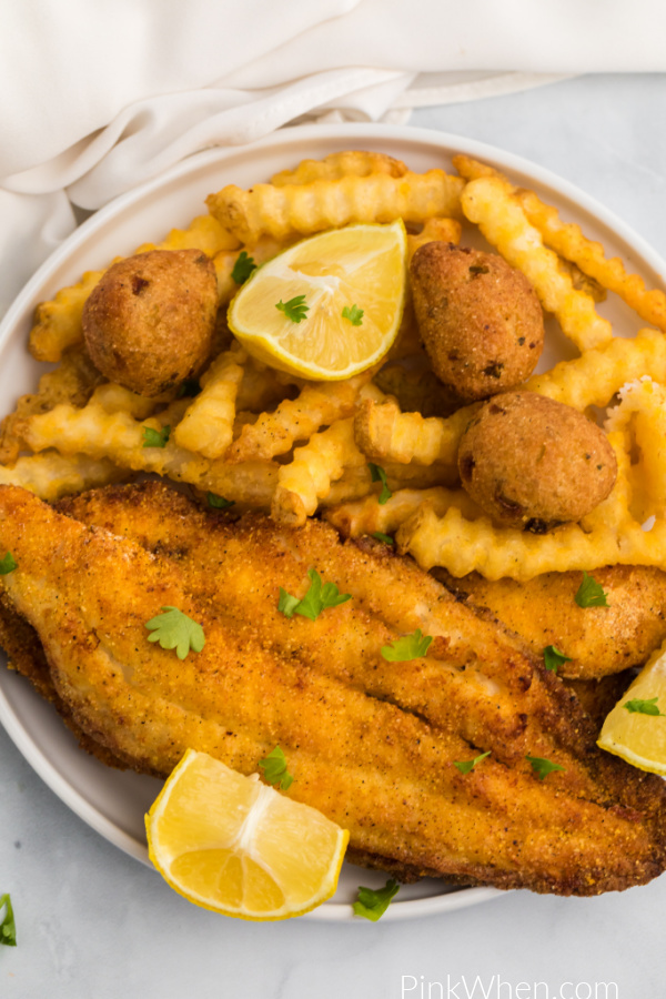 Air Fryer Catfish on a white plate with french fries, hush puppies, and lemon wedges. 