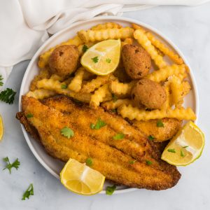 Overhead photo of a plate of catfish made in the air fryer with french fries, lemon wedges, and hush puppies.