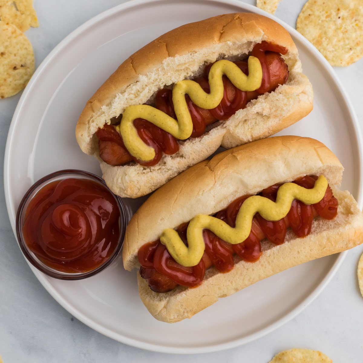 Air Fryer Hot Dogs on a white plate with ketchup and mustard served with extra ketchup