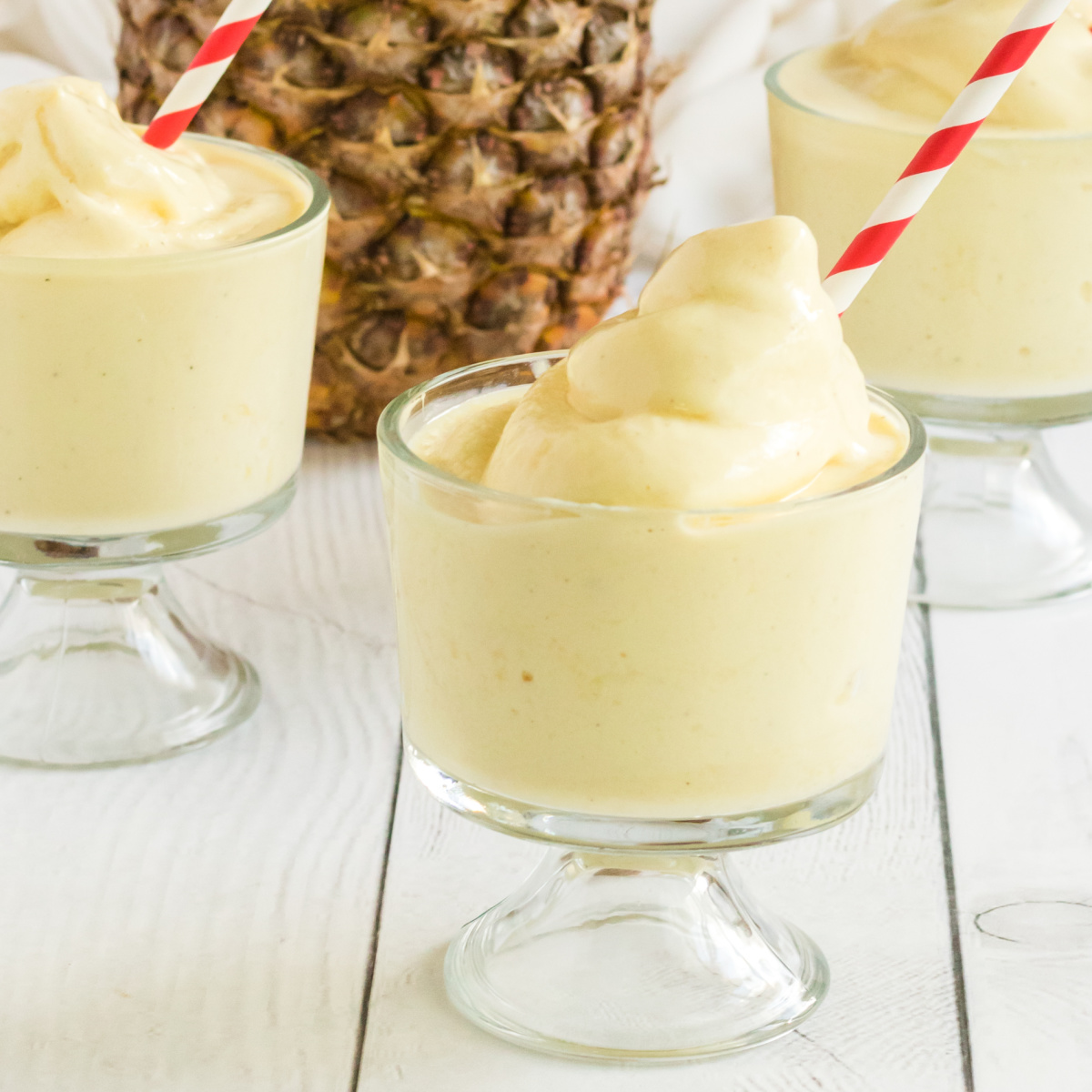 Dole Whip in clear glasses with red and white straws with pineapple in the background