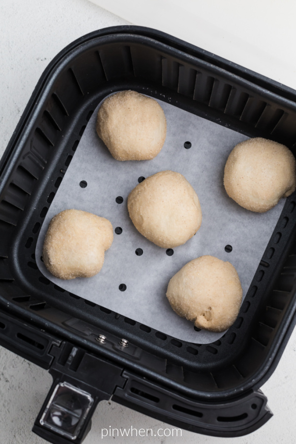 Apple Pie Bombs placed on top of parchment paper in the air fryer basket, ready to cook. 