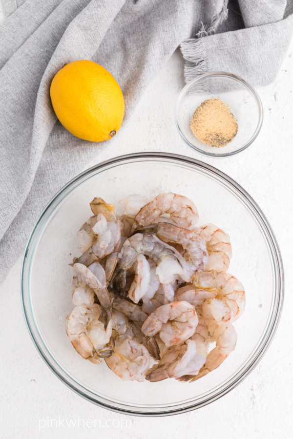 Fresh raw shrimp in a bowl with a lemon and seasonings on a table. 