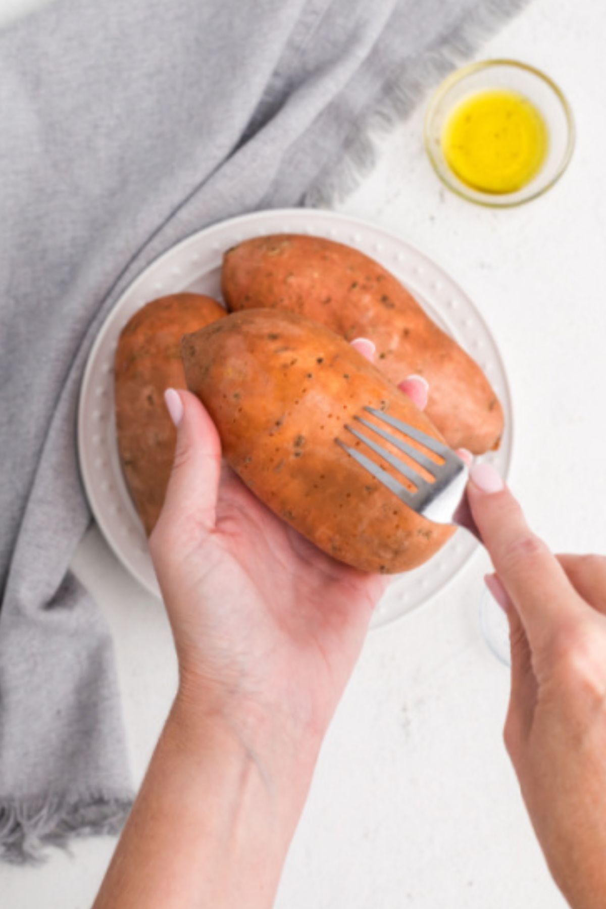 Hand holding a fork, pokeing holes in a sweet potato
