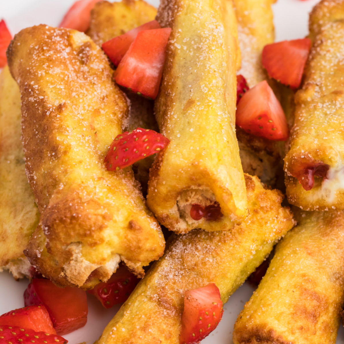 Close up shot of strawberry french toast roll ups stacked on a plate and garnished with strawberries.