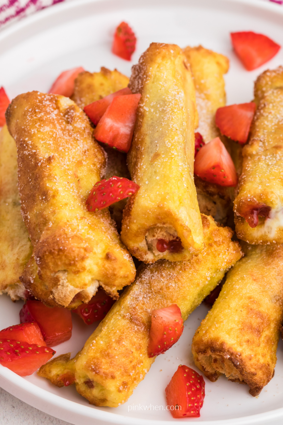 Air Fryer Strawberry French Toast Roll Ups stacked on a plate with chopped strawberries. 