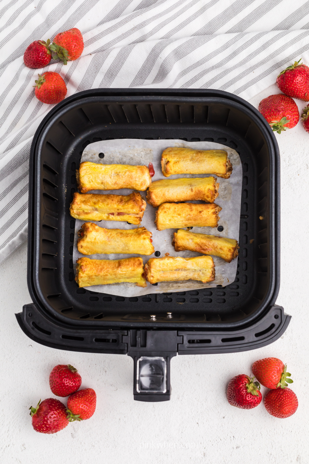 Air Fried French toast roll ups on a piece of parchment paper in the air fryer, ready to serve. 