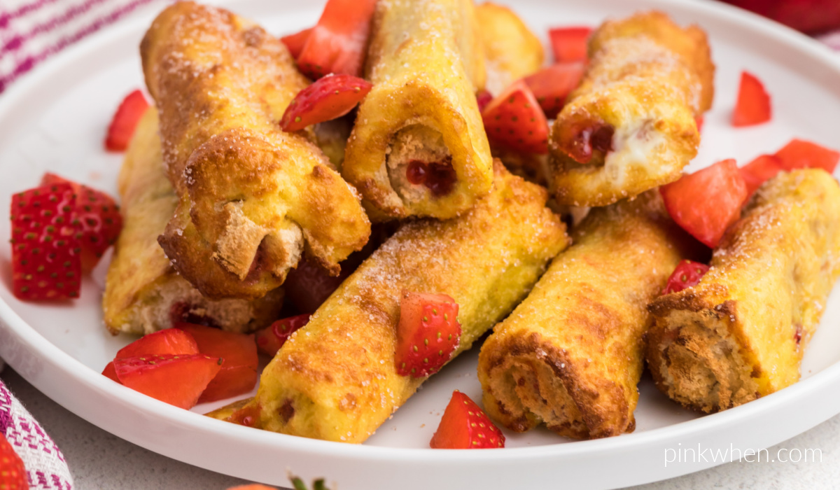 Close up of strawberry french toast roll ups on a white plate and garnished with fresh strawberries. 