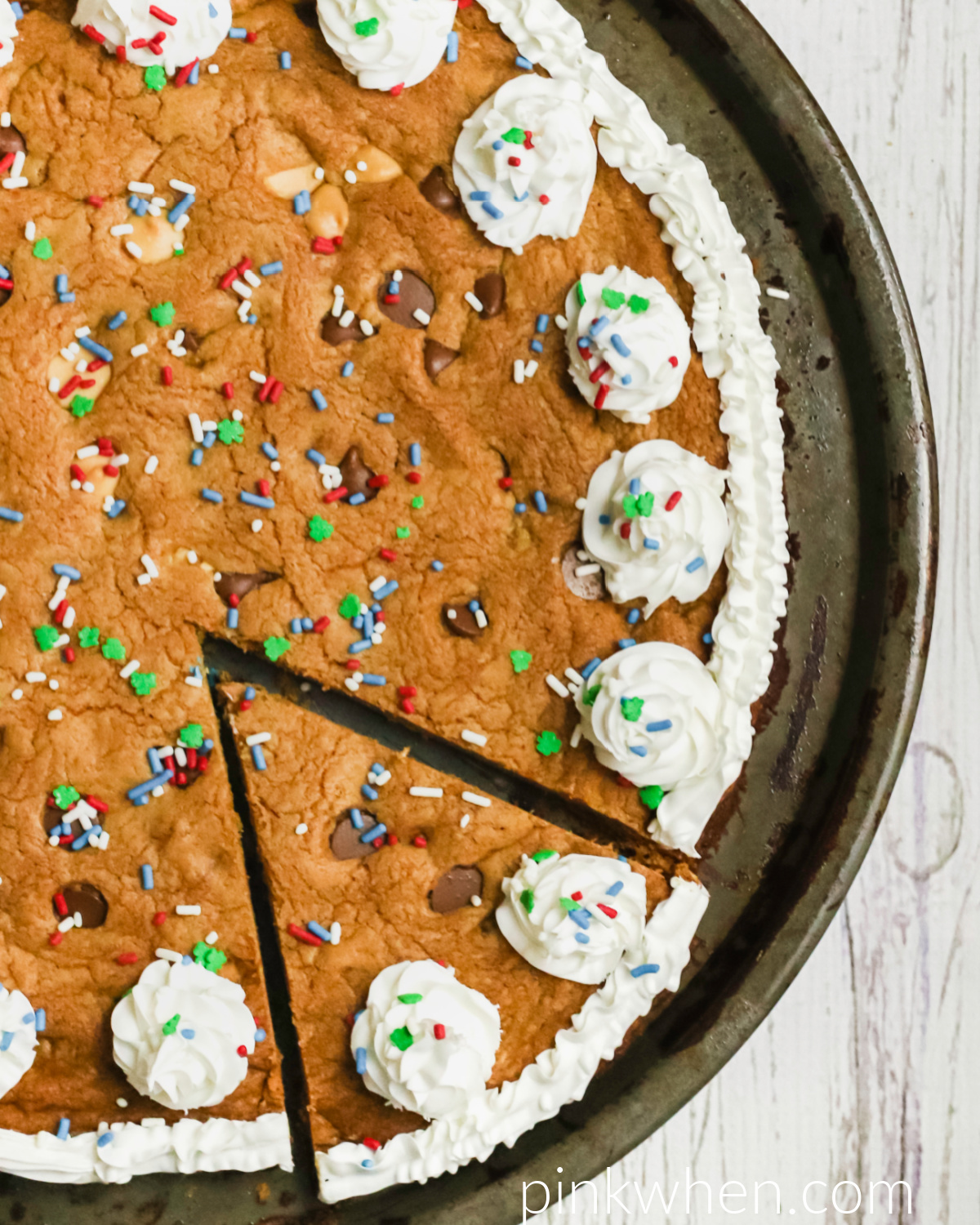 Chocolate Chip Cookie Cake on a pan covered with frosting and sprinkles and with a slice cut to serve. 
