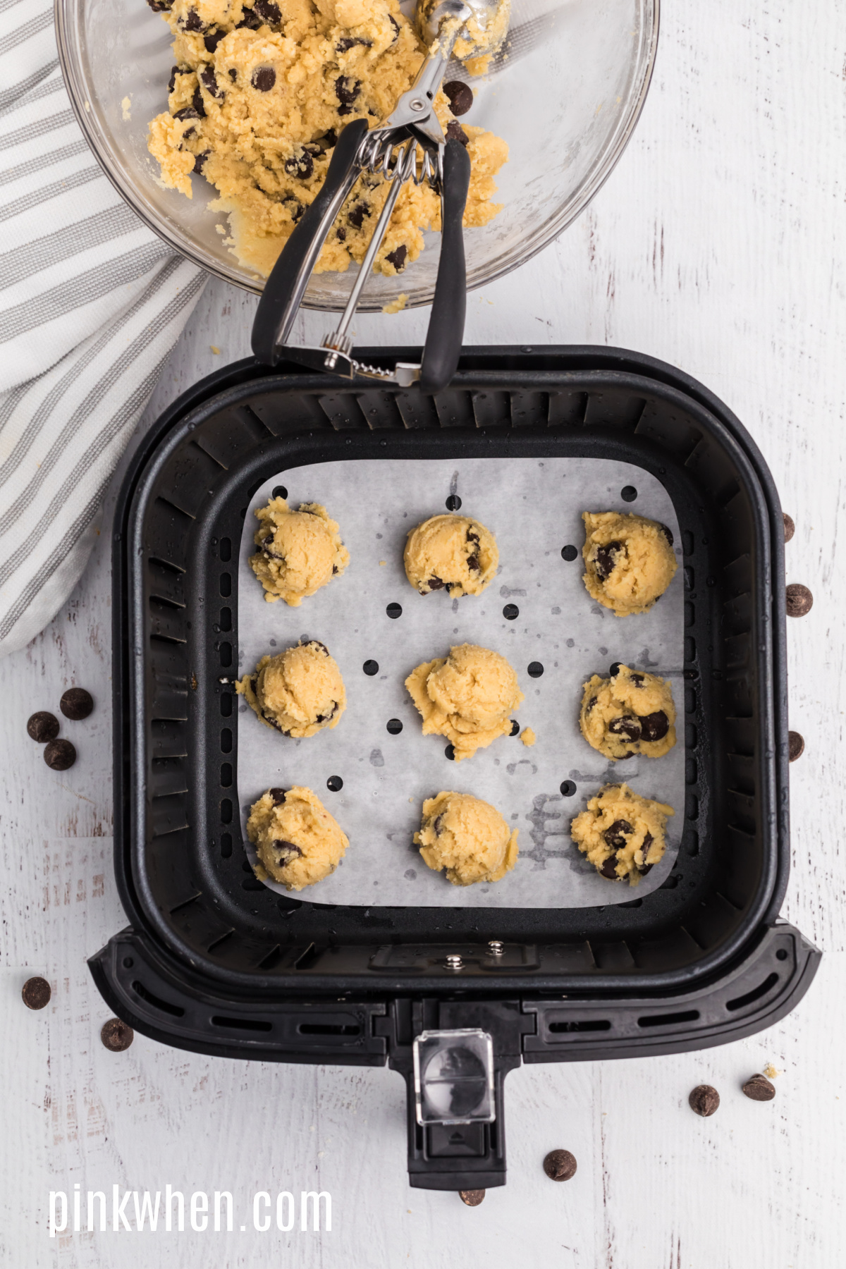 Cookie dough on parchment paper in the basket of the air fryer, ready to bake.