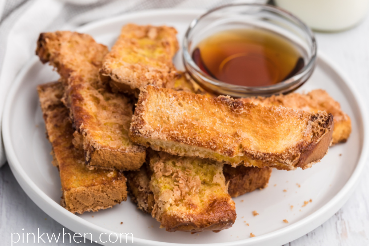Air Fryer French Toast Sticks on a white plate with a small bowl of syrup for dipping. 