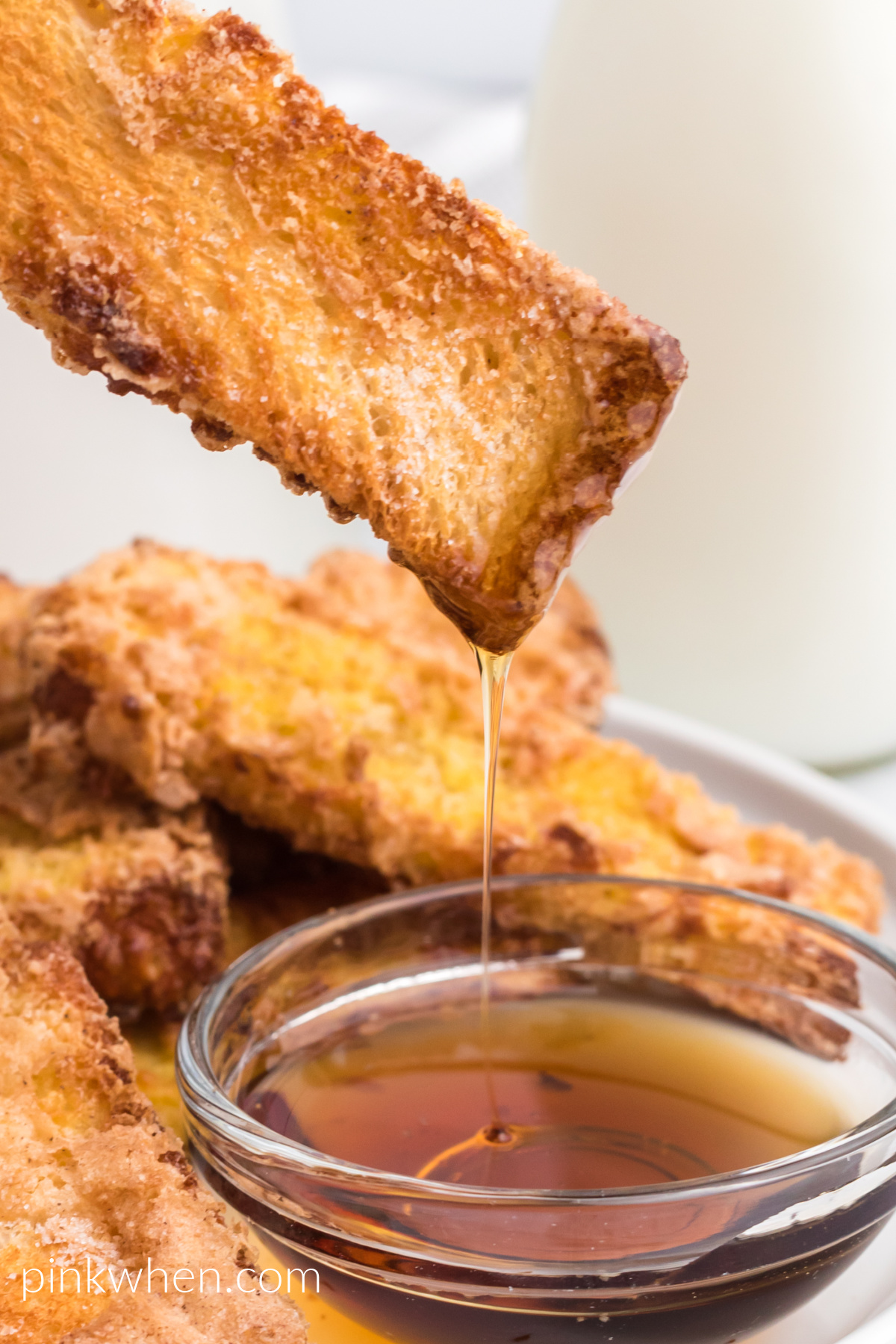 Close up photo of air fryer french toast sticks being dipped in syrup.