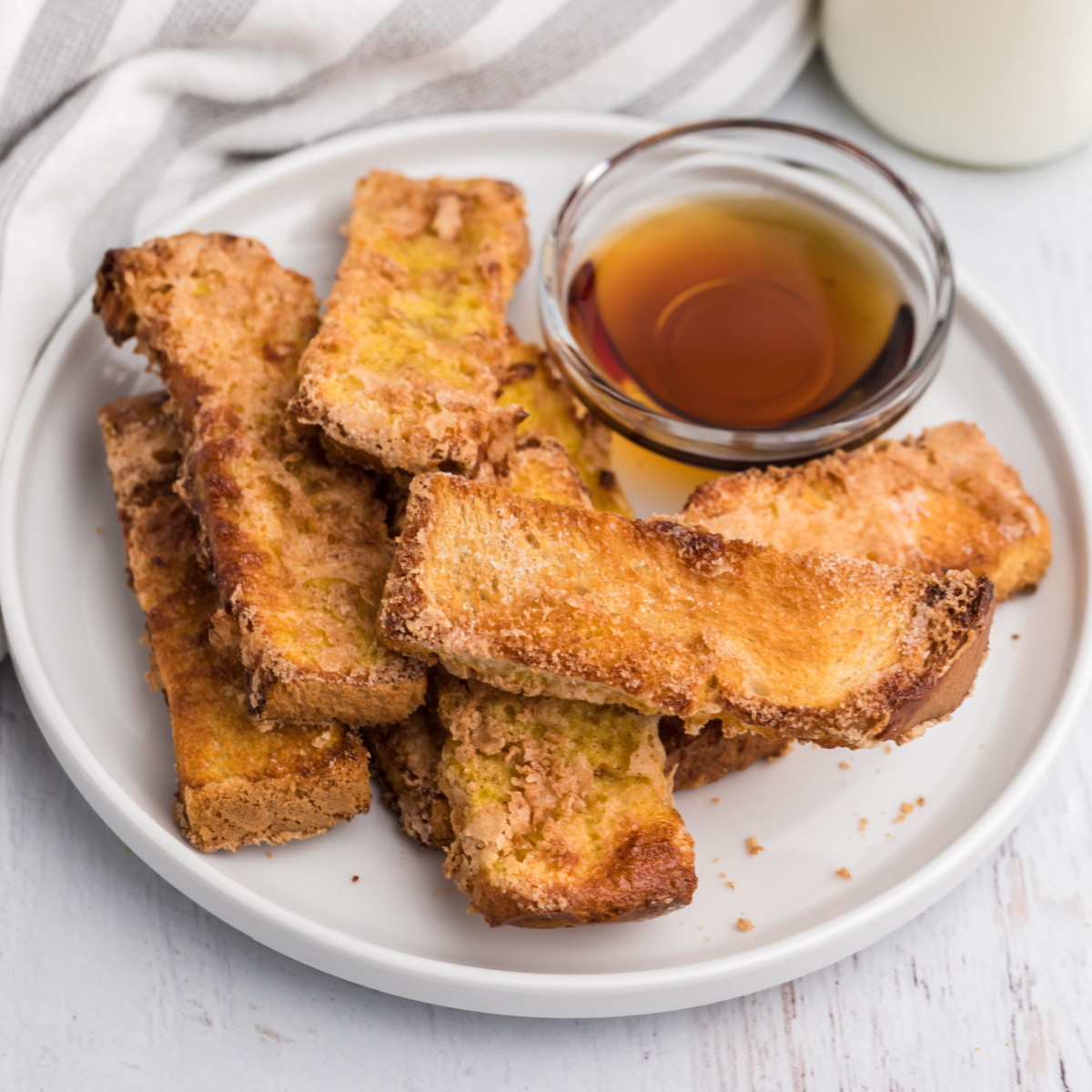 French toast sticks on a white plate with syrup for dipping sauce, ready to eat.