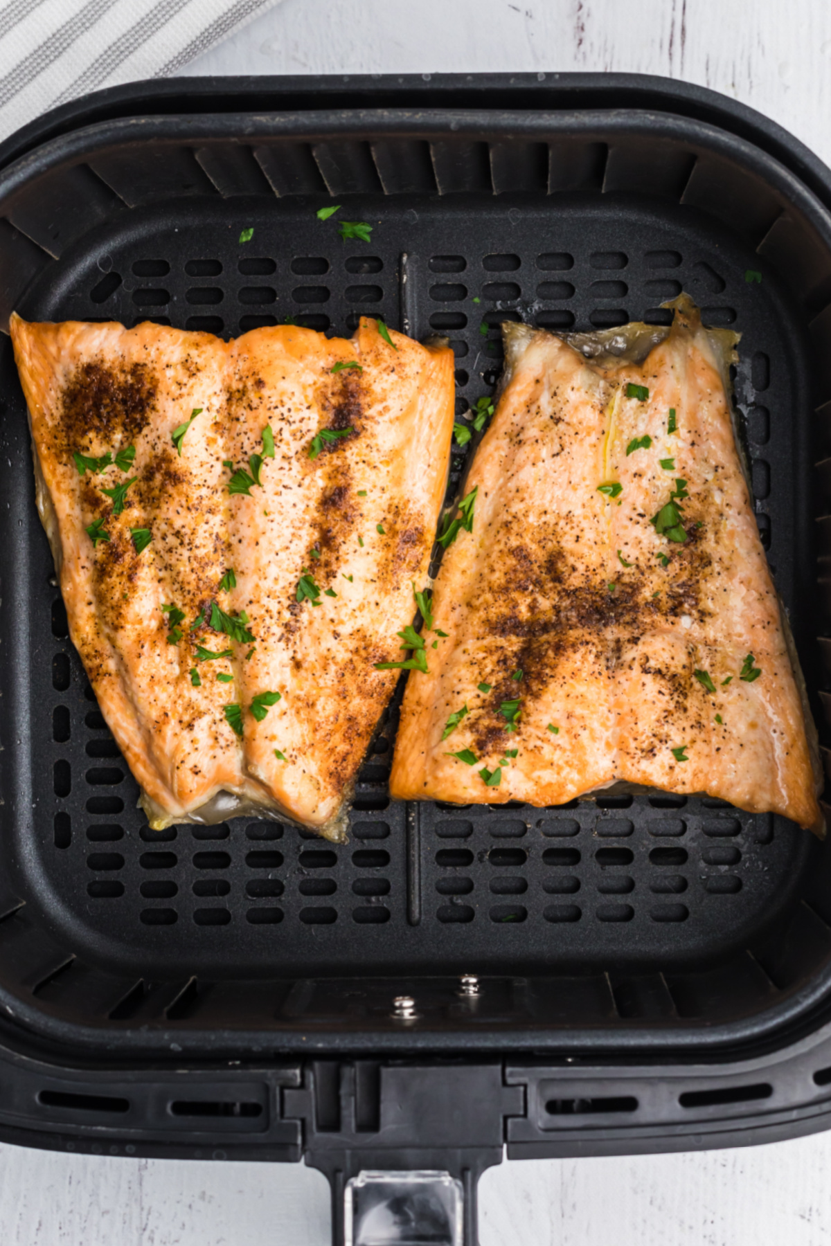 Salmon cooked and served in the basket of the air fryer, ready to be cut and served on a plate.