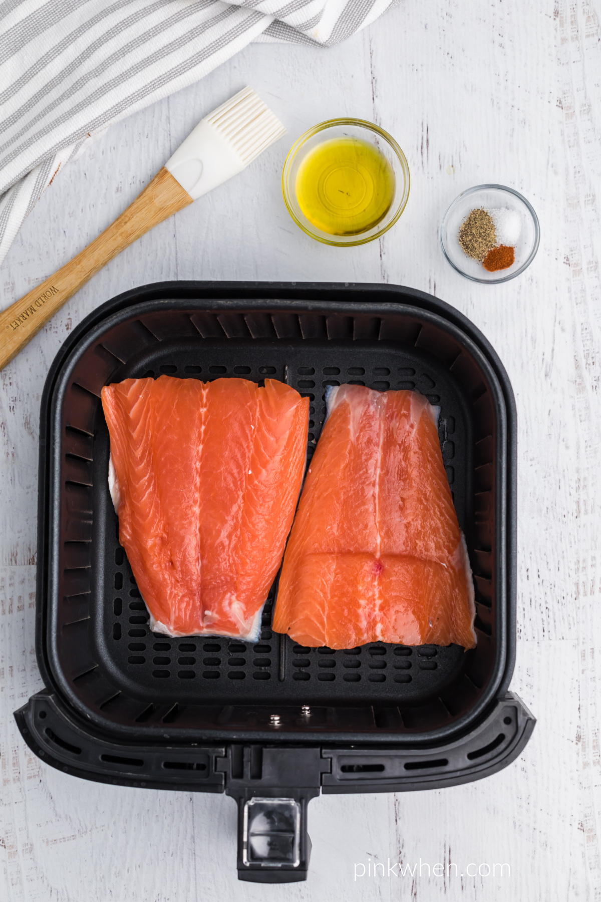 Salmon in the air fryer basket with the seasonings on the side ready to apply. 