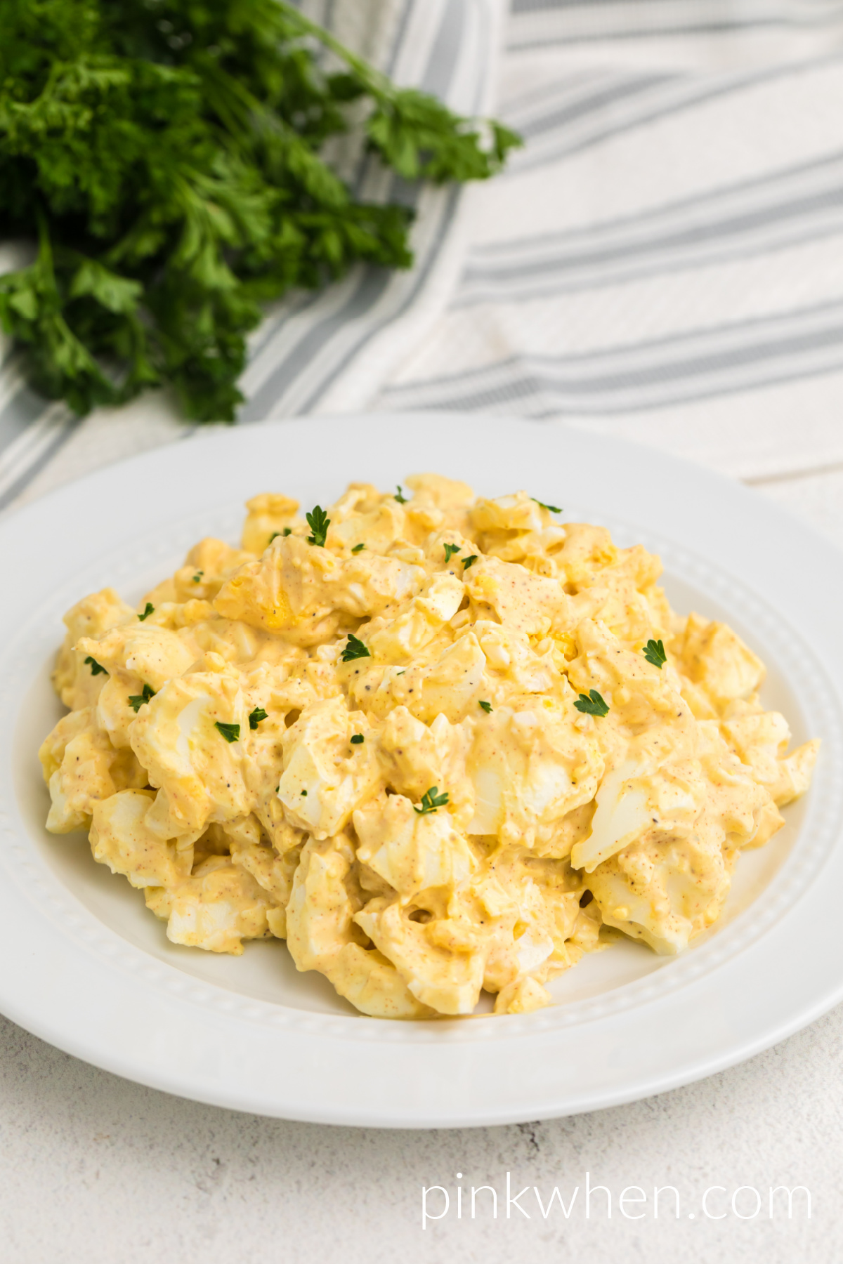Easy egg salad recipe on a white plate and garnished with fresh parsley. 